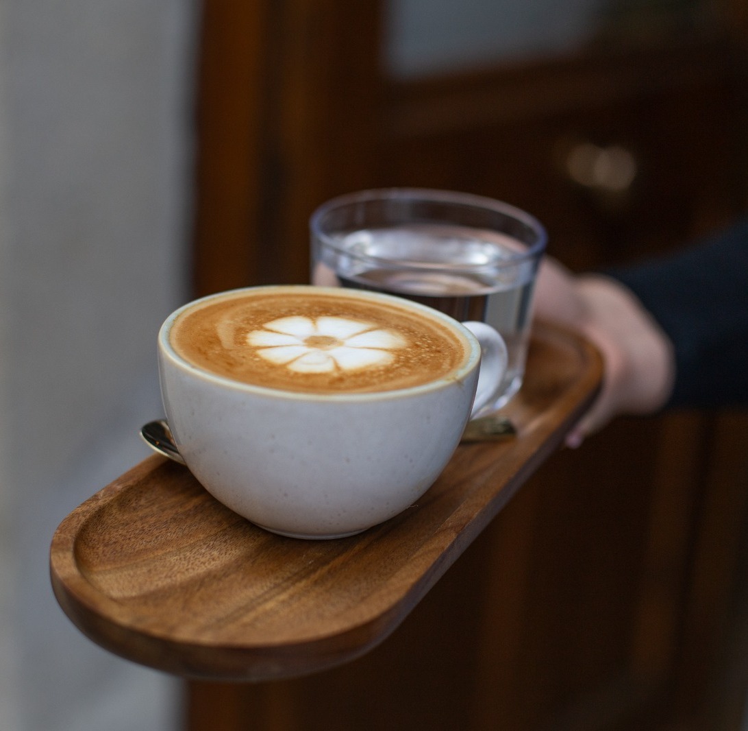 Cappuccino mit Blüten-Latte-Art und Glas Wasser, serviert bei CIN CIN