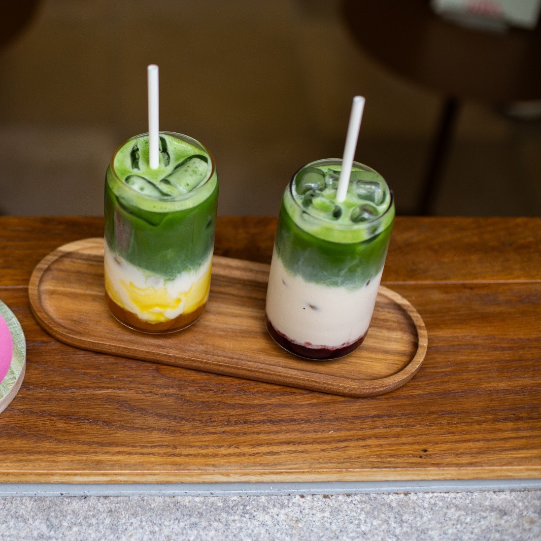Zwei Iced-Matcha-Getränke mit Fruchtsaft-Layer auf Holztablett bei CIN CIN