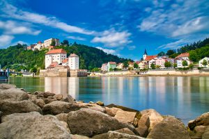 Blick über das Wasser auf die Veste Oberhaus, die Veste Niederhaus und bunte Häuser in Passau