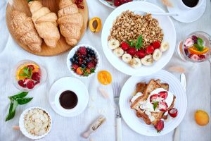 Reichhaltiges Frühstück von oben mit Croissants, Granola mit Banane und Erdbeeren, French Toast und Espresso