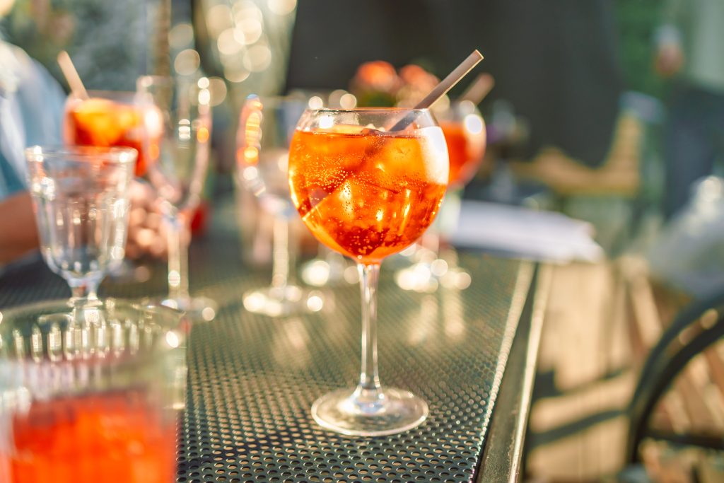 Gekühlter orangefarbener Aperitivo mit Eiswürfeln im Ballonglas auf einem Tisch im Sonnenlicht