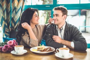 Lachendes Paar im Café bei Kaffee und Tiramisu, sie wischt ihm lächelnd mit einer Serviette über den Mund