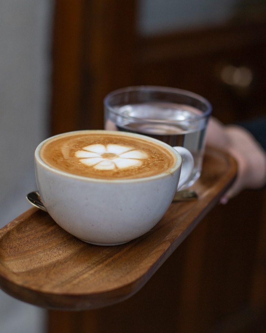 Cappuccino mit Blüten-Latte-Art und Glas Wasser, serviert bei CIN CIN